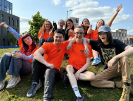 A group of young people attending the Leadership for Life conference 2024 sit on a sunny hillside and pose for a photo