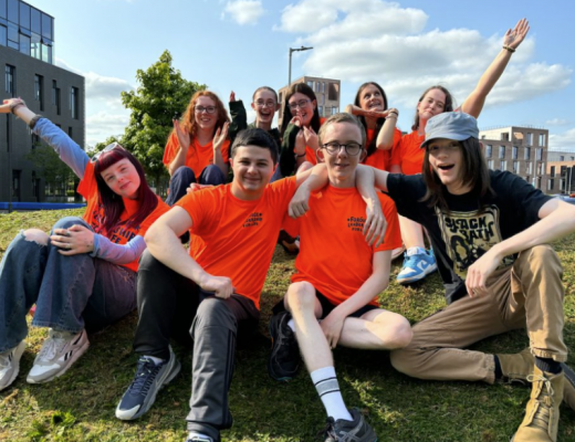 A group of young people attending the Leadership for Life conference 2024 sit on a sunny hillside and pose for a photo