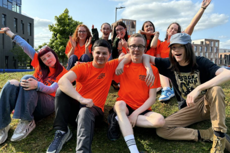 A group of young people attending the Leadership for Life conference 2024 sit on a sunny hillside and pose for a photo